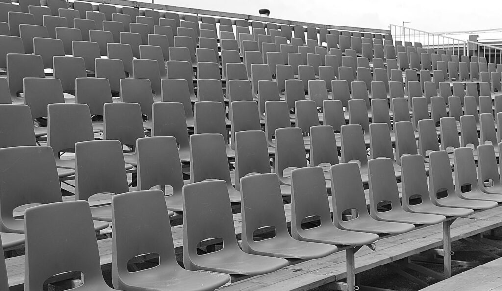 Black and white image of empty stadium bleachers with rows of chairs.